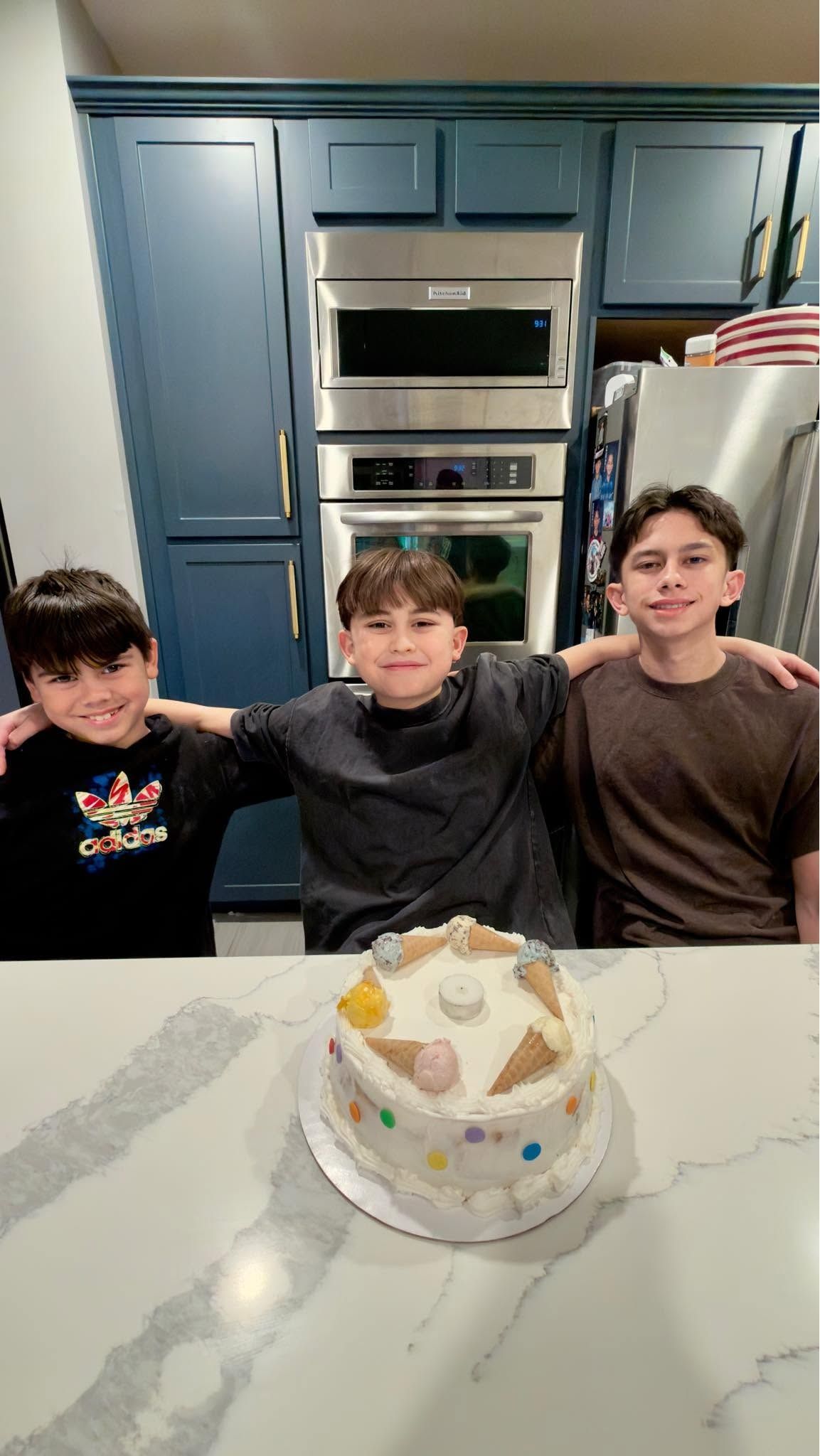 Orion with his two younger brothers at the kitchen counter, arms around each other, with a birthday cake.