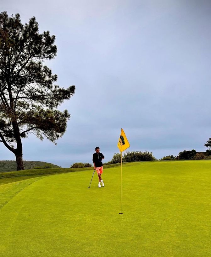 Orion standing on a green beside the flagstick under a big pine tree.